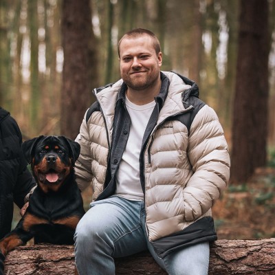 Kieran sitting on a woodland log beside a Rottweiler